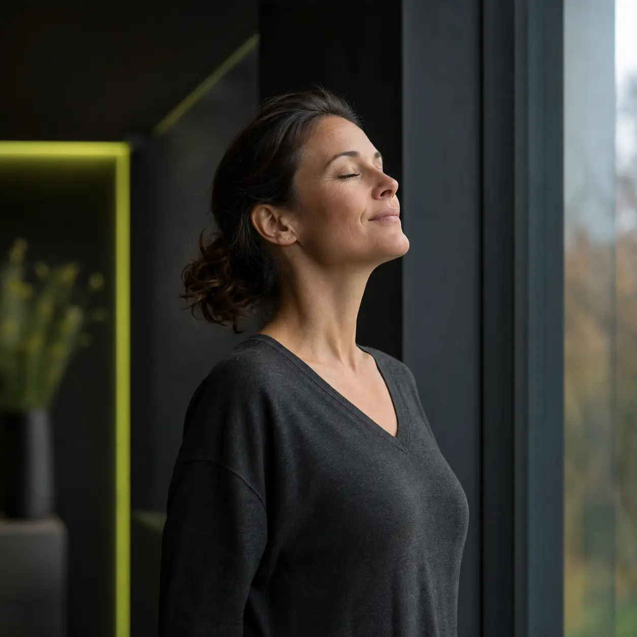 Frau am Fenster einer Cureal Praxis, die nach dem Rauchstopp befreit durchatmet
